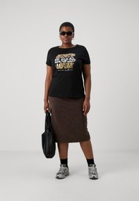 Tricou negru din bumbac cu design imprimat cu animale în auriu și alb, asortat cu o fustă maro, ochelari de soare negri și adidași gri. Geantă neagră.