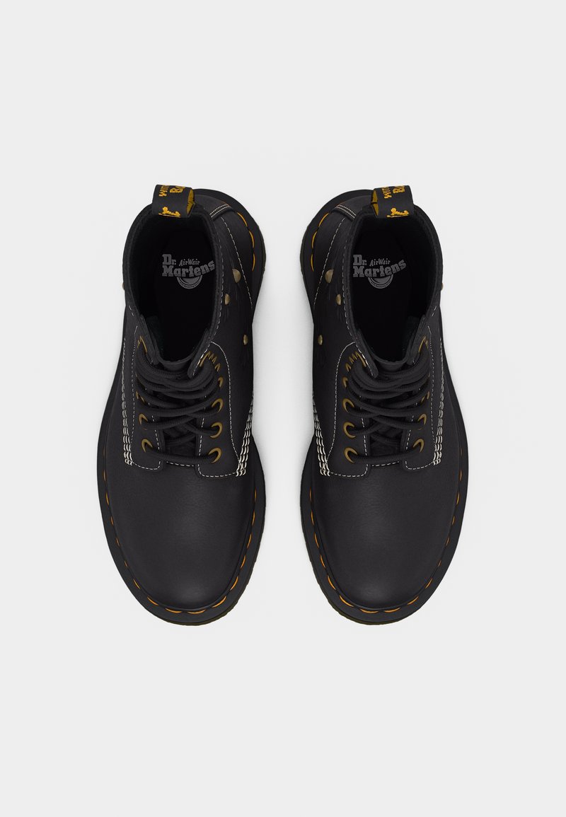 Paire de bottes Dr. Martens en cuir noir avec couture jaune, lacets noirs et languettes de tirage marquées, vues de dessus sur fond blanc.