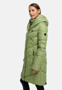 Long green puffer jacket with a hood, featuring quilted texture, snap and zipper closures, and side pockets. Accents include a circular logo on the arm.