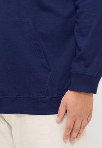 Marineblauwe sweatshirt van zacht stof, met een voorzak, ribbels aan de manchetten en onderkant en minimale stikseldetails.
