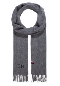 Szary wełniany szalik z frędzlami na końcach, z wyhaftowanym napisem "TH" i małym logo w kolorach czerwonym, białym i niebieskim. Miękka tekstura, prostokątny kształt.