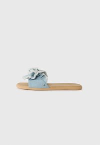 Light blue denim slide sandal featuring ruffled fabric detail, a flat beige sole, and frayed edges on the upper. Simple and open design.