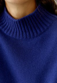 Wollen coltrui in diepblauw, met een geribbelde kraag en een gladde textuur, met een close-up van de details van de stofweving.