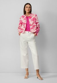 Veste rose à motif floral sur un haut rose vif, assortie à un pantalon blanc et des talons beiges à lanières. Présente une coupe courte et des boutons.