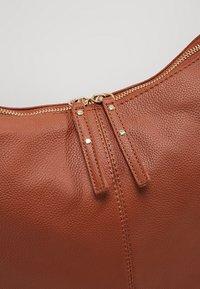 Ruskea nahkalaukku, jossa on teksturoitu pinta, varustettu kahdella vetoketjuhangalla ja kultasävytteisellä metalliosalla vetoketjun sulkemisessa ylhäällä.