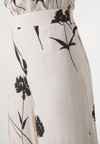 Rok met bloemendruk in lichtbeige stof, voorzien van zwarte bloemenpatronen, zachte textuur en een tailleband met lichte plooien.