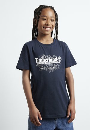 T-shirt en coton bleu marine avec un graphique de montagne blanche et le texte "Timberland". Manches courtes, encolure ronde, coupe décontractée.