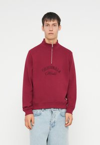Hanorac bordo cu guler înalt și fermoar pe jumătate, având un logo embossat "ORIGINALS". Material moale și croială relaxată.