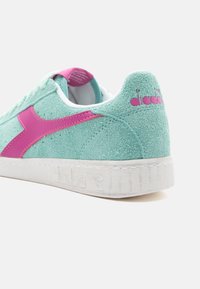 Svijetloplave suede tenisice s roza logotipom i detaljima. Imaju teksturiranu površinu i bijelu gumenu potplatu s rebrastim detaljima.