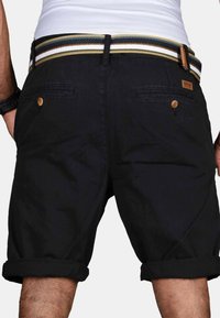 Man wearing rolled-up black shorts with back buttoned pockets and a striped belt, seen from behind at waist level.