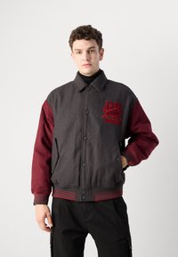 Men's bomber jacket featuring a gray wool blend body, maroon sleeves, ribbed cuffs, and an embroidered logo on the chest.