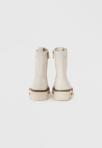 Botines crema con textura suave, suela marrón y detalle de cremallera lateral. Cuentan con punta redonda y forro suave para mayor comodidad.