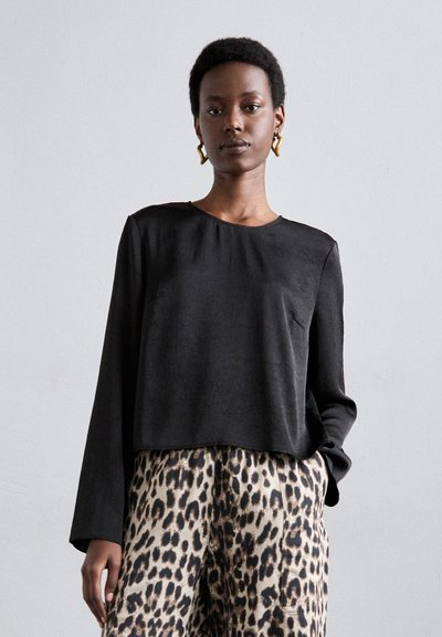 Bluză lungă neagră cu mâneci lungi și gât rotund, dintr-un material texturat, asortată cu pantaloni bej cu un model de leopard întunecat.