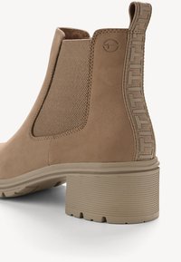 Bottes de cheville en daim tan avec des panneaux élastiques latéraux, des accents texturés et un talon en caoutchouc épais. Présente une logo sur le côté et une semelle crantée.