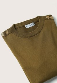 Pull vert olive plié soigneusement, avec un col rond, une texture côtelée et deux boutons métalliques sur l'épaule. Le tissu semble doux.