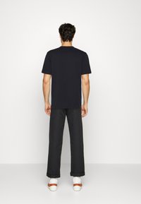 Camiseta azul marino de manga corta, vista desde la parte de atrás. Combinada con pantalones negros y zapatos blancos con un detalle de correas marrones.