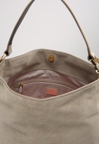 Grote beige suède totebag met een glad interieur, voorzien van een ritssluitingvak en gouden hardware accenten. Ruim en zachte textuur.