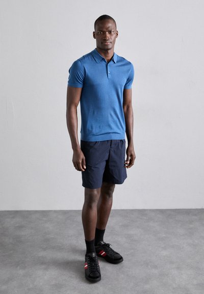 Meeste sinine lühikeste varrukatega polo särk, valmistatud siledast kangast; kaasneb tumesiniste lühikesed püksid ja mustad tossud punaste detailidega.