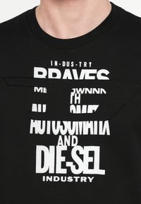 Čierne bavlnené tričko s veľkým bielym nápisom, okrúhlym výstrihom a výrezom pri oblasti hrudníka. Nápisy obsahujú názvy značiek a frázy.