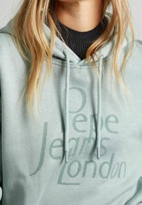 Felpa con cappuccio verde menta con coulisse, tasca a marsupio e logo "Pepe Jeans London" stampato in un audace tono più scuro.