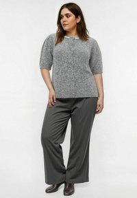 Maglione grigio lavorato a maglia con maniche corte e tessuto testurizzato, abbinato a pantaloni larghi a righe grigie e stivali alla caviglia marrone scuro.