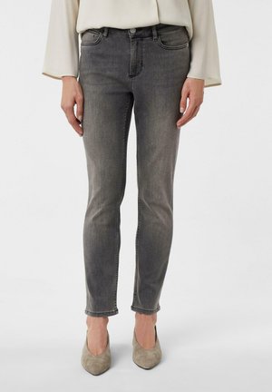 Graue Jeans im Skinny Fit mit mittlerer Taille, subtilen Verwaschungen, genähten Details und knöchellangen Säumen, kombiniert mit taupefarbenen High Heels.