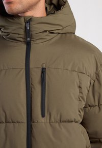 Olive green puffer jacket featuring a hood, black zipper, and a side pocket with a zip closure. Soft texture with quilted design.