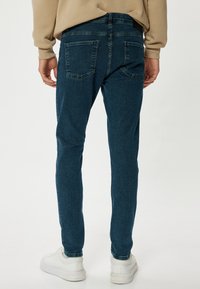 Slim-fit siniset farkut, valmistettu joustavasta kankaasta, joissa on kaksi takataskua ja keskikorkea vyötärö, yhdistettynä valkoisiin tennareihin.