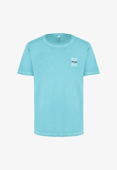 T-shirt in cotone turchese con scollo rotondo, maniche corte e una piccola etichetta bianca sul petto che mostra il nome del marchio "Moschino."