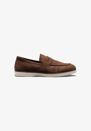 Mocassin en daim marron avec une semelle en caoutchouc blanche, style sans lacets, et une bride décorative sur le dessus.