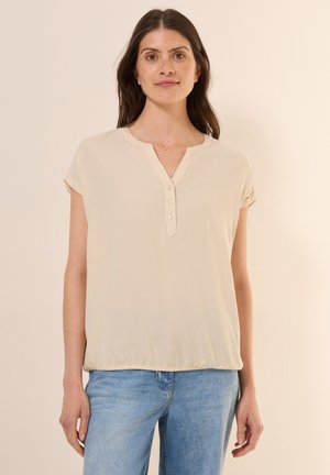 Beige Bluse mit kurzen Ärmeln und V-Ausschnitt, dreiknöpfiger Frontblende und sanft gerafftem Bund. Weiche, glatte Stofftextur.