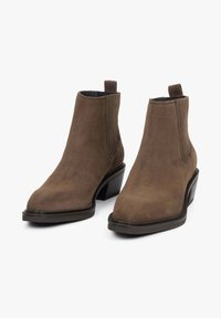 Brązowe zamszowe botki za kostkę z zaostrzonym noskiem, elastycznymi panelami po bokach i niskim, zdobionym obcasem. Gładka faktura z minimalnymi detalami metalowymi.