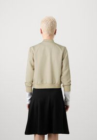 Beige bombardérka s elastickým pasem a manžetami, zkombinována s černou rozšířenou sukní, pohled zezadu.