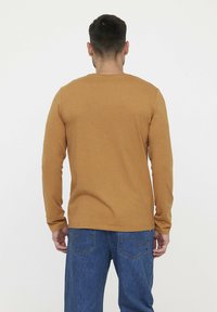 Langarm shirt van zacht, mosterdgele stof met een ontspannen pasvorm en een ronde halslijn, gecombineerd met blauwe denim jeans.