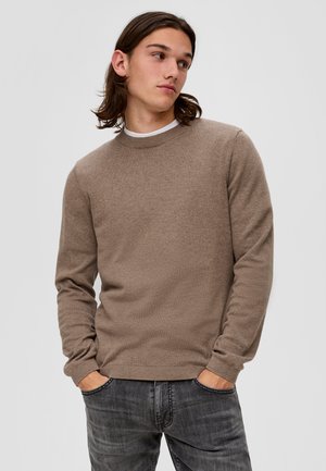 Bruine ronde hals trui, gebreide textuur, lange mouwen, geribbelde manchetten en zoom. Draagt over een wit shirt, gecombineerd met donkere jeans.