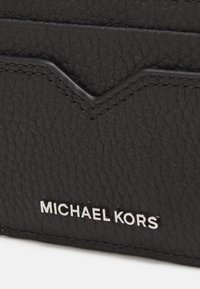 Porte-carte en cuir noir avec une finition texturée, un accent en forme de V et un détail de marque en argent près du bas.