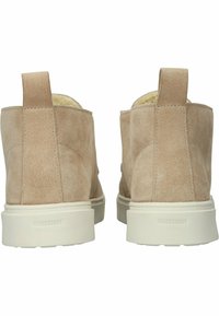 Botas de tobillo de ante beige con punta redonda, acabado texturizado, lengüetas en la parte posterior y suela de goma blanca. Logo "BLACKSTONE" en el talón.
