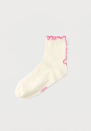 Chaussette chevillère en coton crème avec un bord supérieur froncé rose et un logo rose sur le côté. Texture douce et coupe extensible.