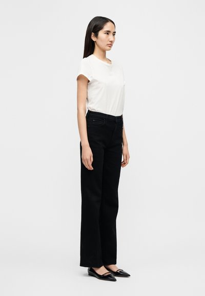 Λευκό t-shirt με κοντά μανίκια, μαύρο παντελόνι ίσιας γραμμής και μαύρες μπαλαρίνες. Μινιμαλιστικός σχεδιασμός με απλή σιλουέτα κ αι απαλή υφή υφάσματος.