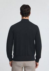 Svart tröja med hög krage, ribbstickade muddar och nederkant. Mjuk textur med figursydd design, visad bakifrån mot en ljus bakgrund.