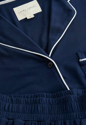 Mornarska pižama s belimi robovi, ki vključuje ovratnik s klini, enojno zaponko in elastičen pas. Gladka tekstura tkanine.