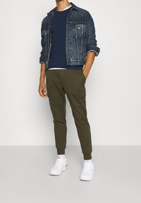 Jeansjacka, marinblå crew neck-tröja, olivgröna cargo-joggers och vita sneakers. Outfiten har en avslappnad passform och kontrasterande texturer.