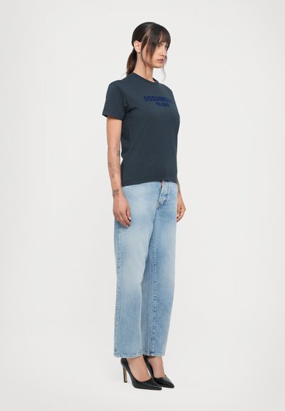 Marineblauwe t-shirt met korte mouwen met de opdruk "DSQUARED2 MILANO", gecombineerd met lichtblauwe rechte jeans en zwarte hoge hakken.