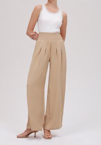Beżowe spodnie o szerokich nogawkach z teksturowanym wykończeniem i plisami z przodu. Połączone z dopasowanym białym topem z prążkowanej dzianiny i cielistymi szpilkami.