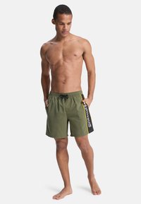 Shorts de bain vert olive avec une taille à cordon, des poches latérales et le logo "Quiksilver" en blanc sur une bande noire.