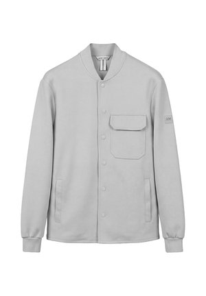 Chaqueta abotonada de color gris claro con un bolsillo de solapa en el pecho, dos bolsillos laterales, puños acanalados y un pequeño parche en la manga izquierda.