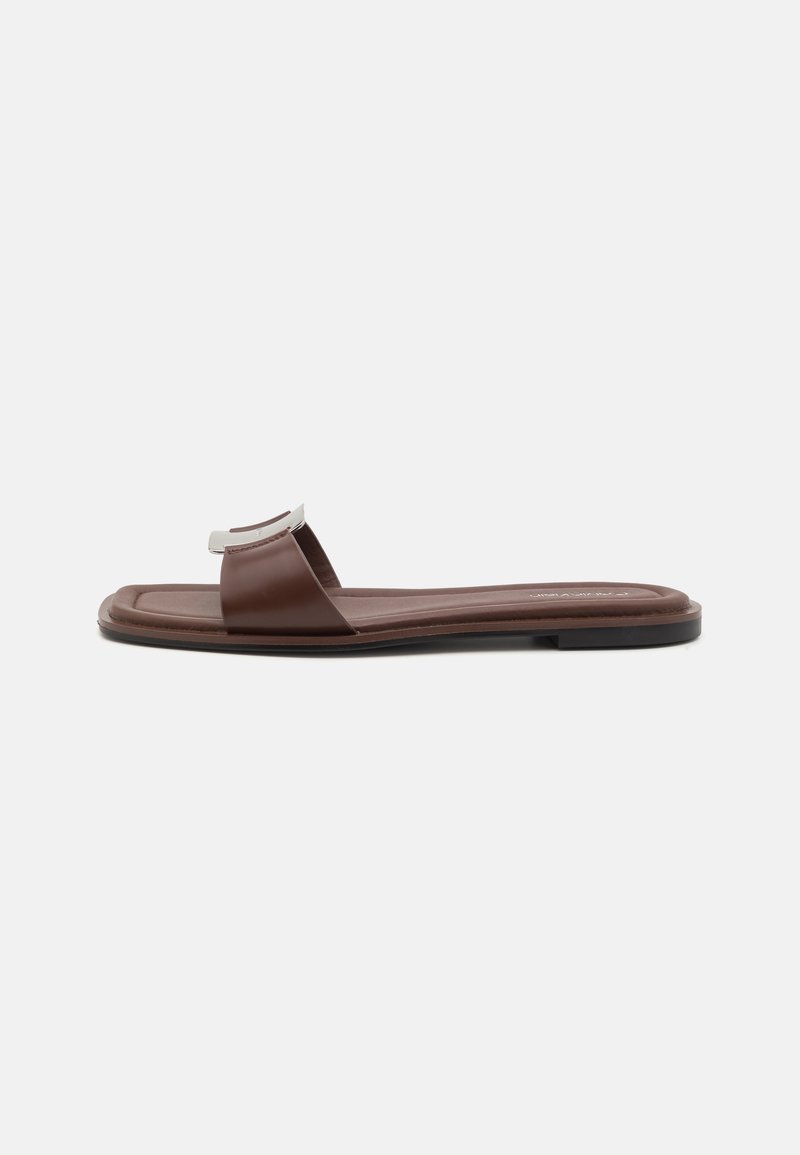 Brun slidesandal med en rem som har en silveraccent. Platt design med en mjuk textur, bred fotbädd och minimalistisk profil.