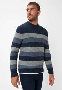 Pullover a righe blu e grigie in maglia testurizzata, caratterizzato da un collo a giro e polsini e orlo a coste. Indossato con jeans scuri.
