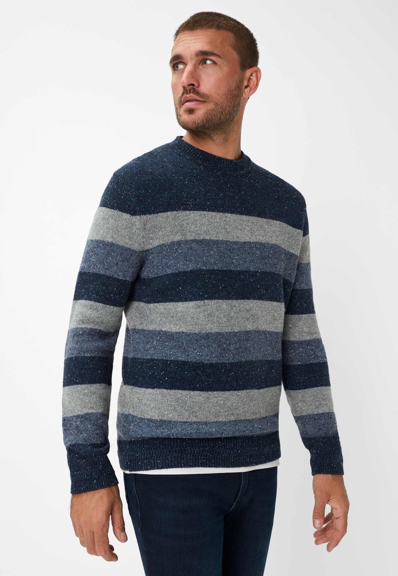 Pullover a righe blu e grigie in maglia testurizzata, caratterizzato da un collo a giro e polsini e orlo a coste. Indossato con jeans scuri.