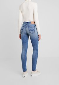Smala blå jeans med en tvättad look, fem fickor och en brun läderlapp i bakre midjan. Bärs med en krämfärgad långärmad topp.